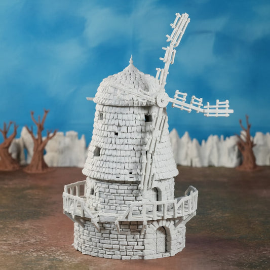 Graue verfallene Windmühle aus Stein mit zerbrochenen Flügeln auf braunem Boden vor blauem Himmel.